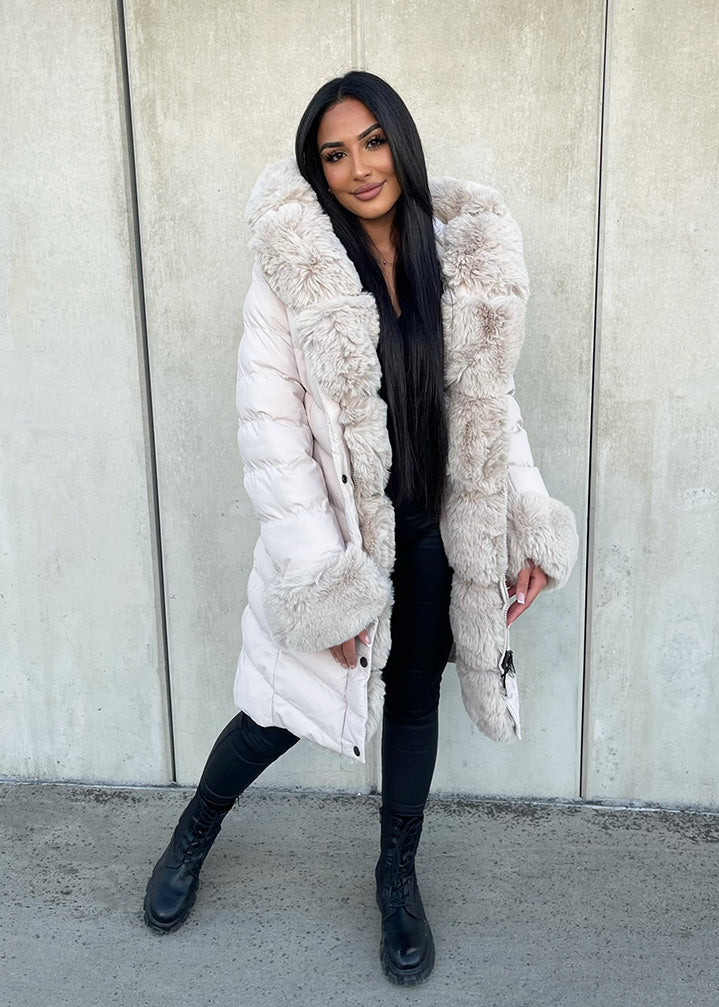 Modell trägt eine taillierte Damen Steppjacke mit Gürtel, Fellkragen und Fellärmeln – NAHA Wintermode