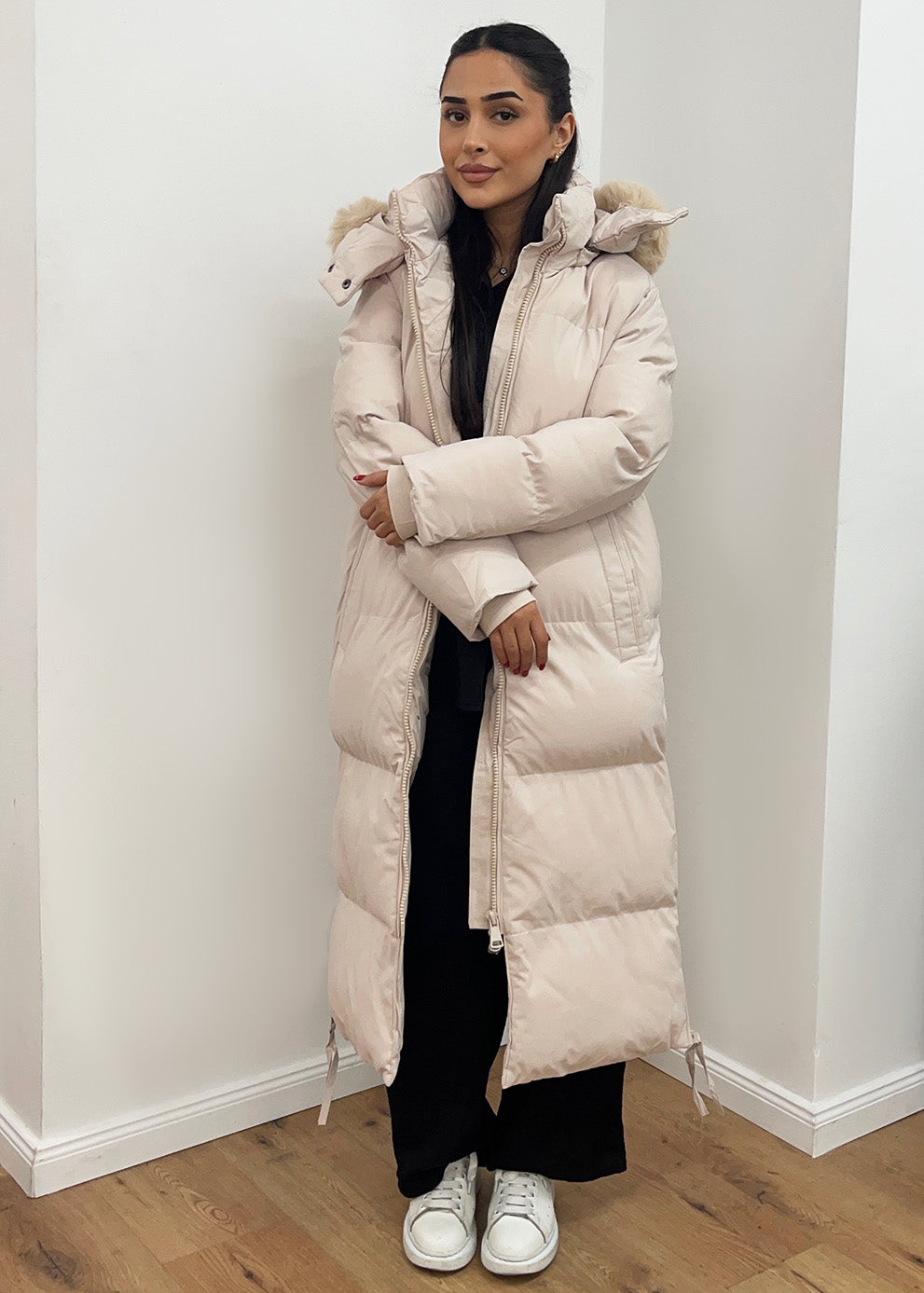 Modell trägt einen langen Damen Steppmantel mit Kapuze und seitlichen Reißverschlüssen – NAHA Wintermode