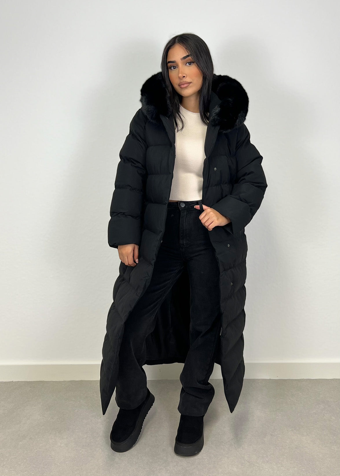 Modell trägt einen langen Damen Steppmantel mit Kapuze und Taillengürtel – NAHA Wintermode