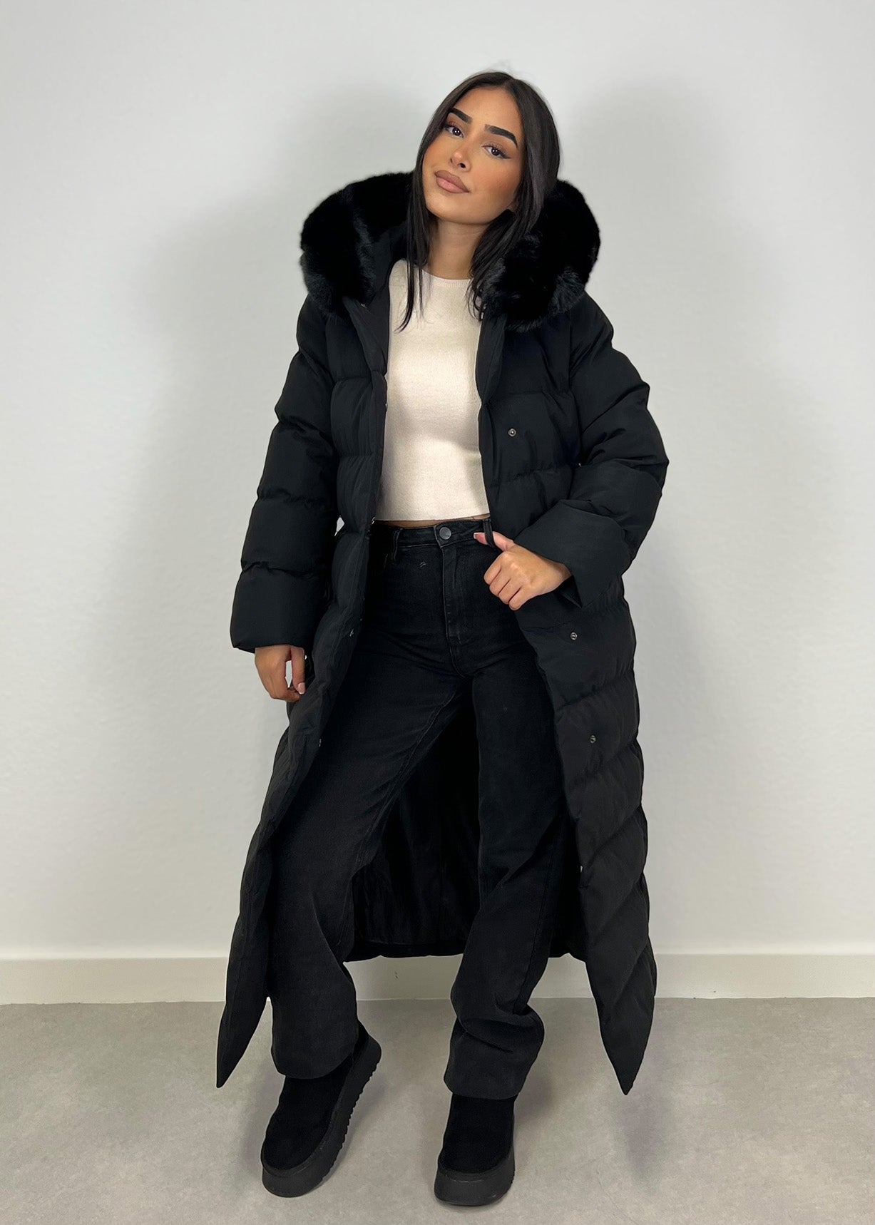 Modell trägt einen langen Damen Steppmantel mit Kapuze und Taillengürtel – NAHA Wintermode