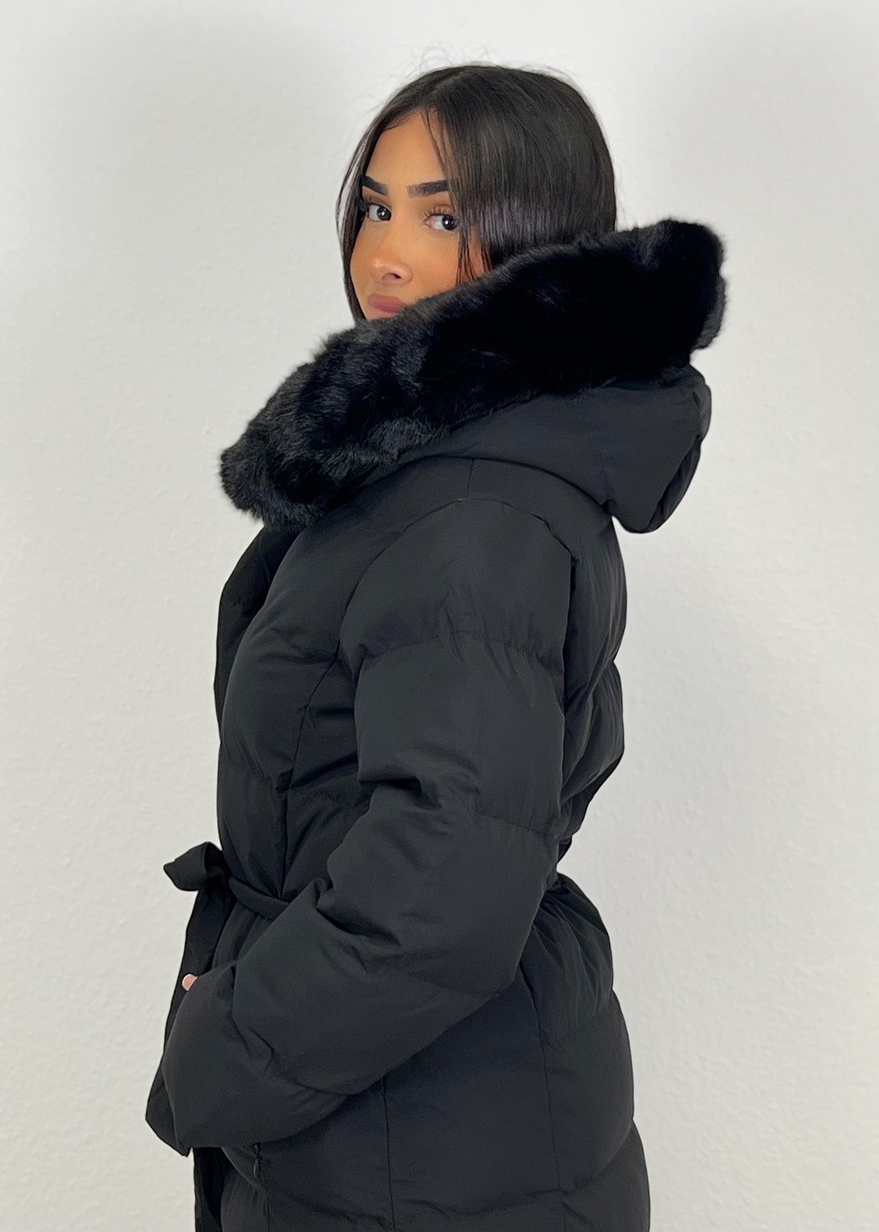 Modell trägt einen langen Damen Steppmantel mit Kapuze und Taillengürtel – NAHA Wintermode