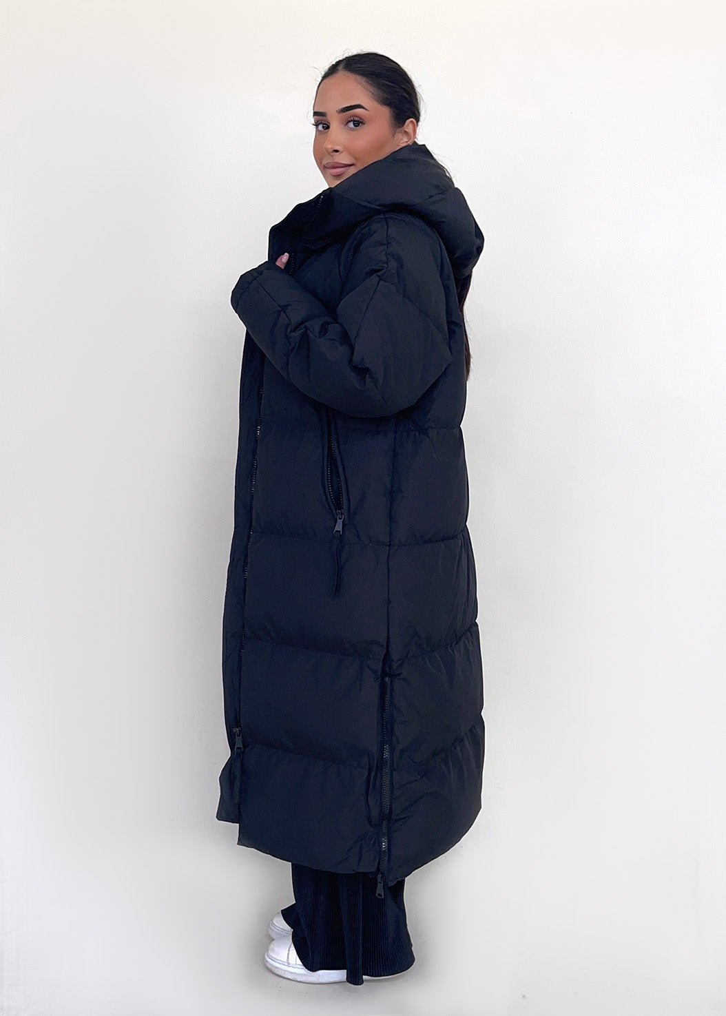 Modell trägt einen langen Damen Steppmantel mit Kapuze und durchgehendem Reißverschluss – NAHA Fashion