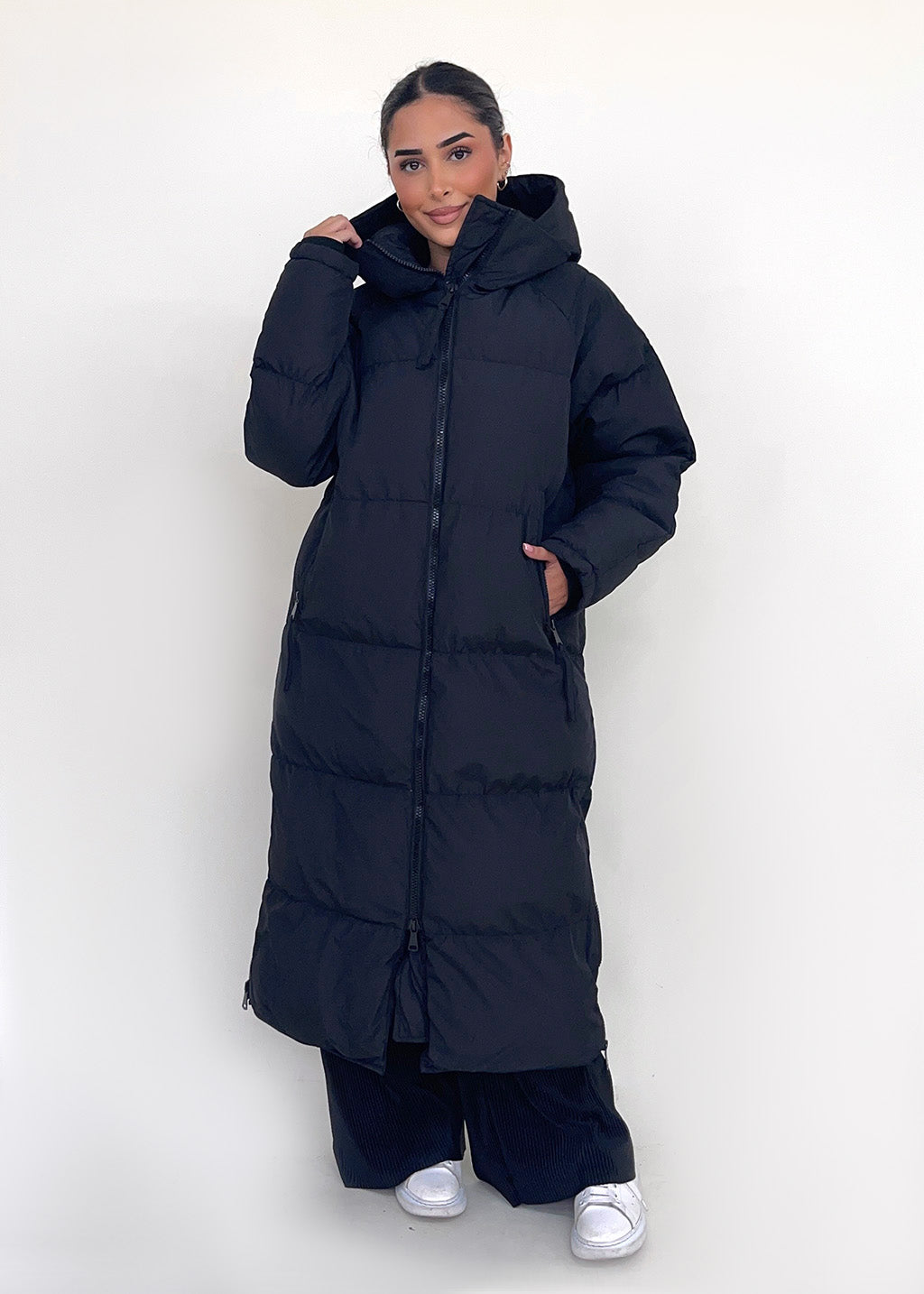 Modell trägt einen langen Damen Steppmantel mit Kapuze und durchgehendem Reißverschluss – NAHA Fashion