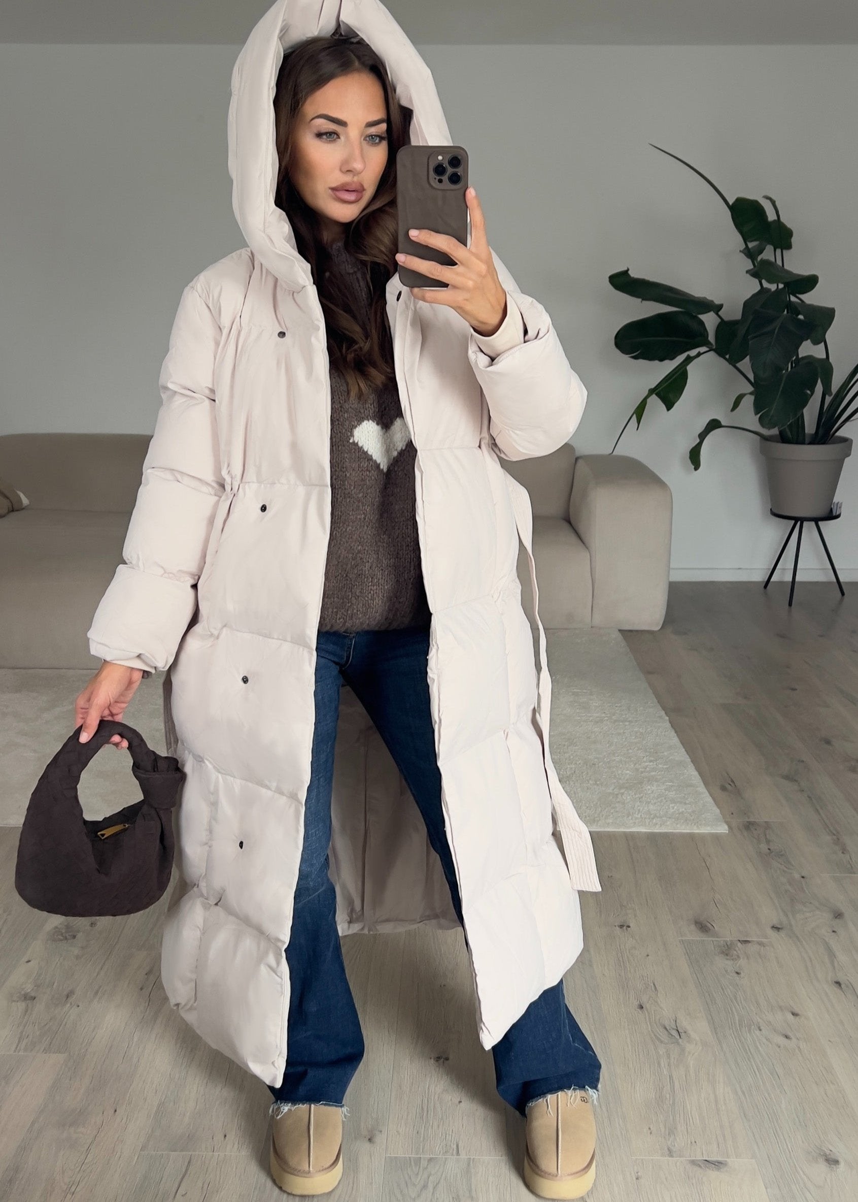 Modell trägt einen langen Damen Steppmantel mit Kapuze und Taillengürtel – NAHA Wintermode