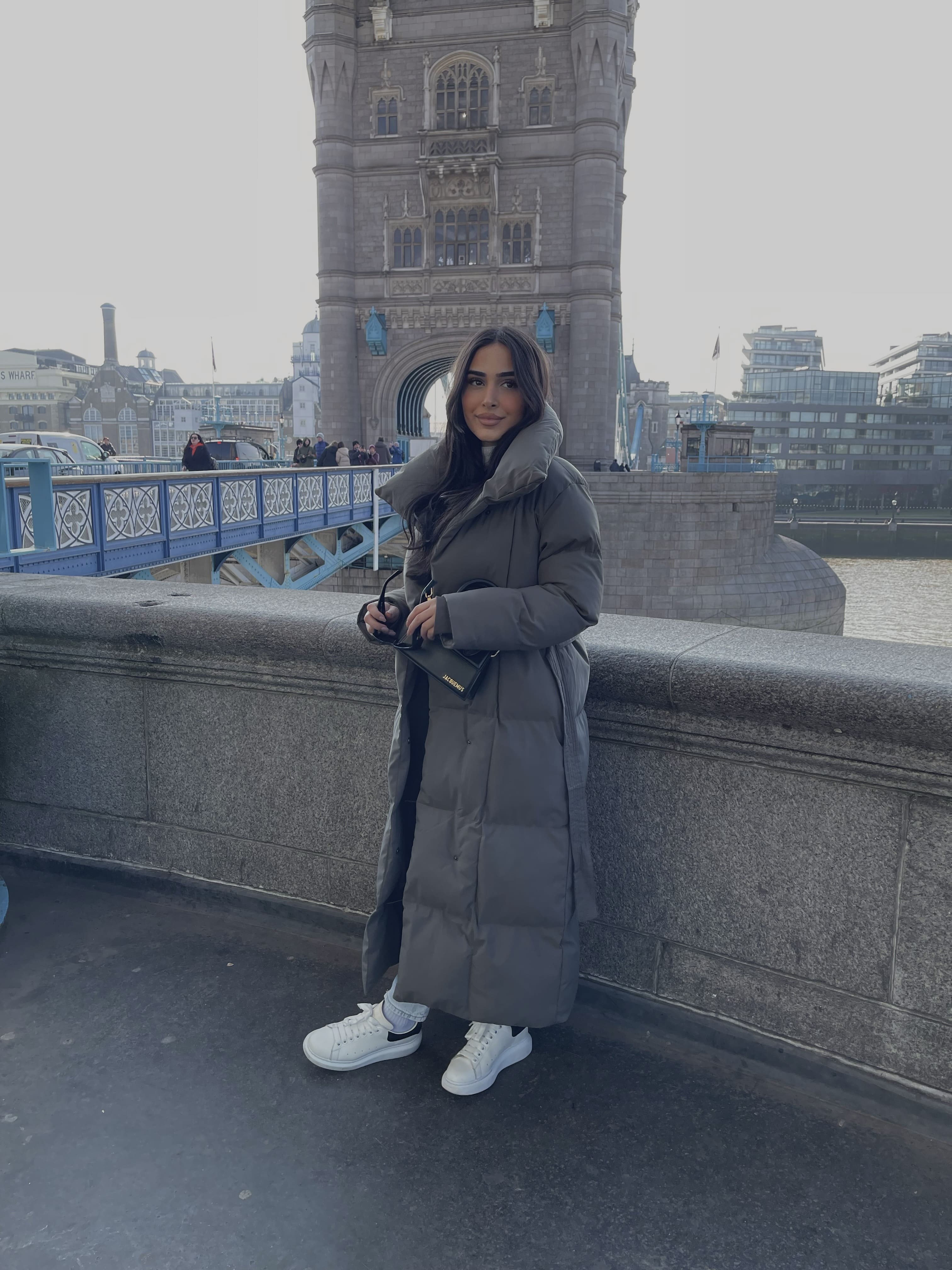 Frau trägt lange graue Winterjacke mit Gürtel & Stehkragen – moderner Winterlook von NAHA