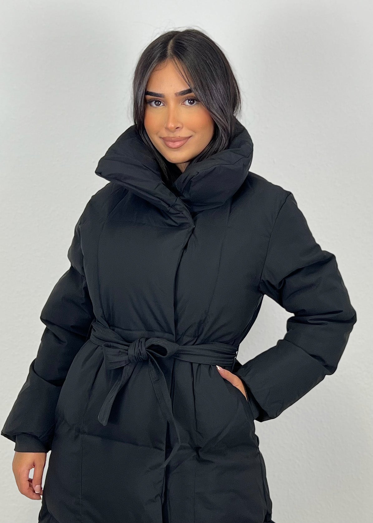 Frau trägt lange Winterjacke in Schwarz mit Gürtel & hohem Kragen – eleganter Winterlook von NAHA