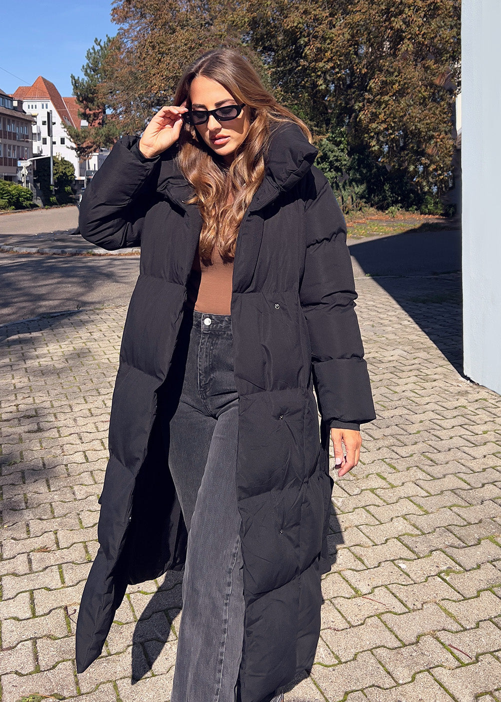 Frau trägt lange Winterjacke in Schwarz mit Gürtel & hohem Kragen – eleganter Winterlook von NAHA