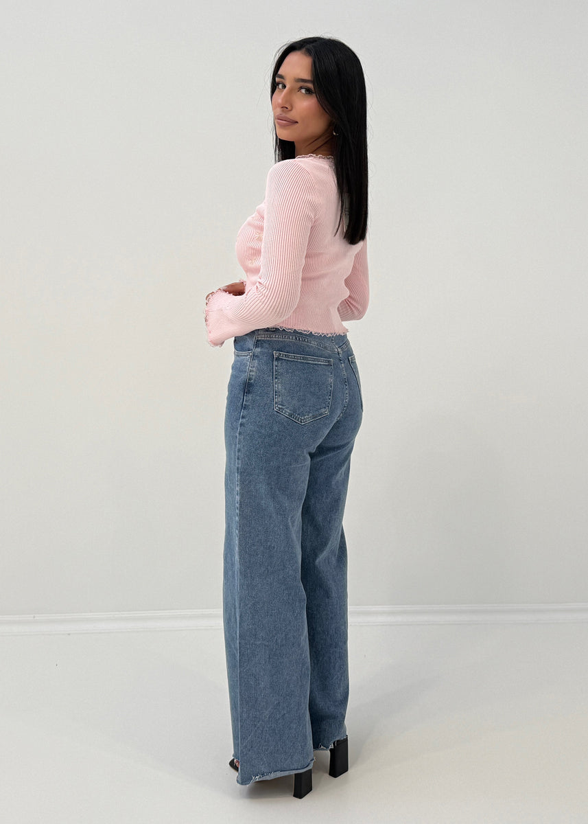 Modell trägt Langarm-Ripp-Oberteil mit Zierschleifen und ausgestelltem Ärmelabschluss