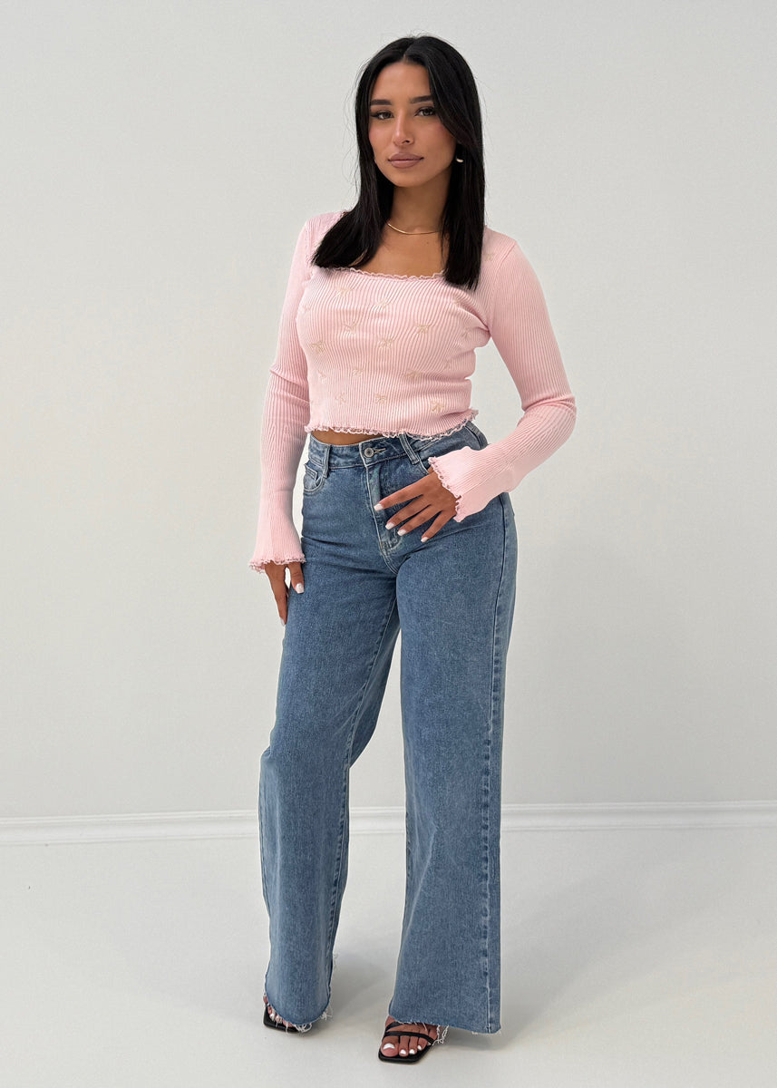 Modell trägt Langarm-Ripp-Oberteil mit Zierschleifen und ausgestelltem Ärmelabschluss