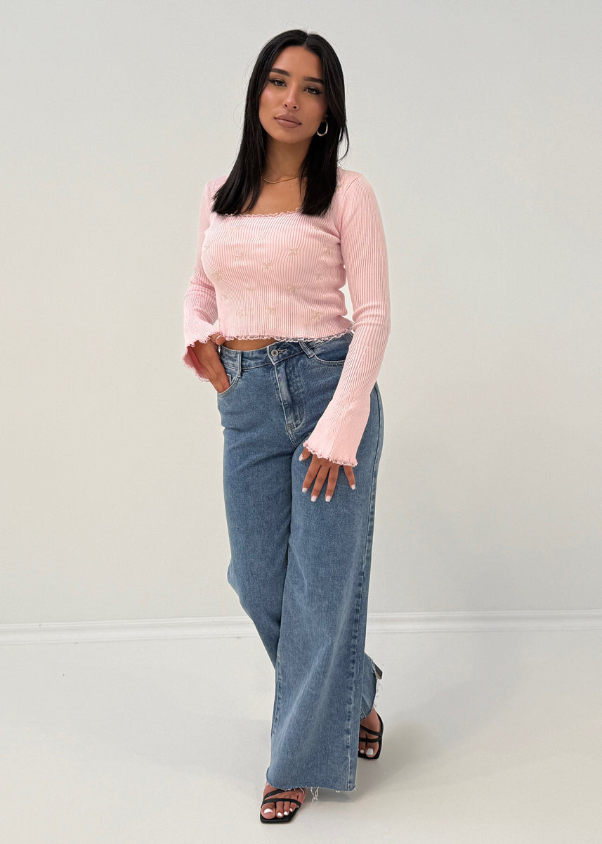 Modell trägt Langarm-Ripp-Oberteil mit Zierschleifen und ausgestelltem Ärmelabschluss