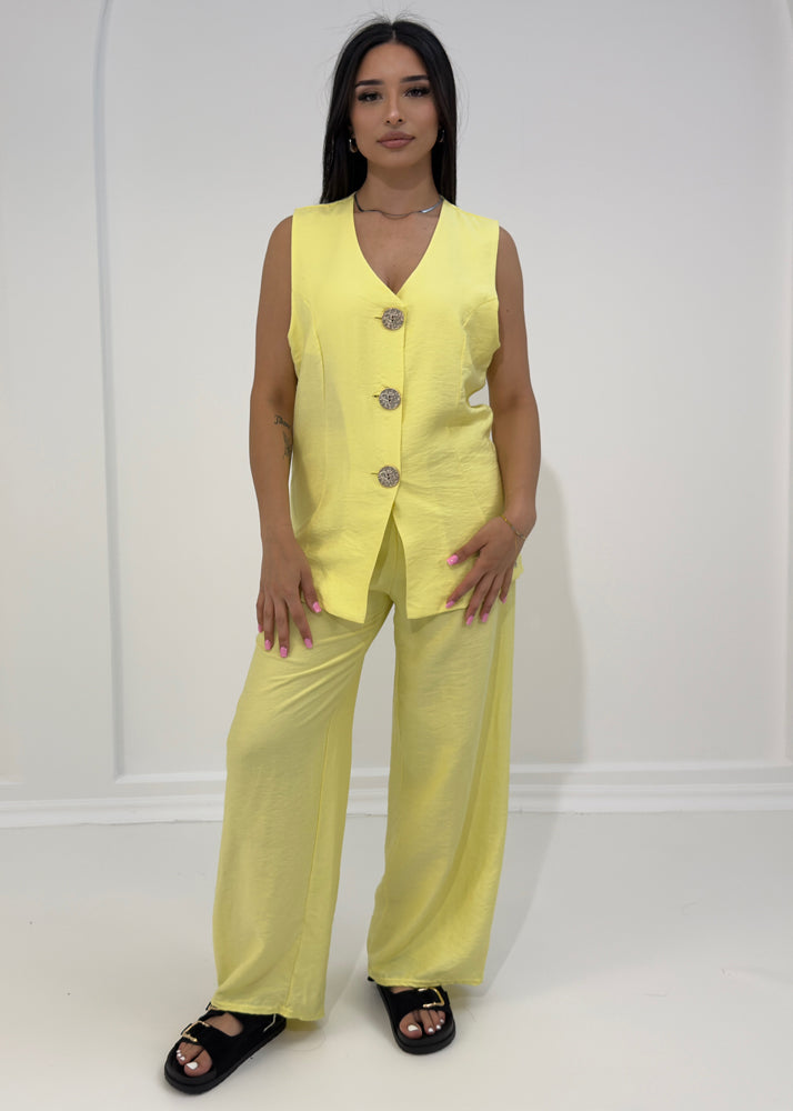 Frau trägt ärmellosen Zweiteiler mit goldenen Knöpfen und weiter Hose – eleganter Sommerlook aus der NAHA Kollektion