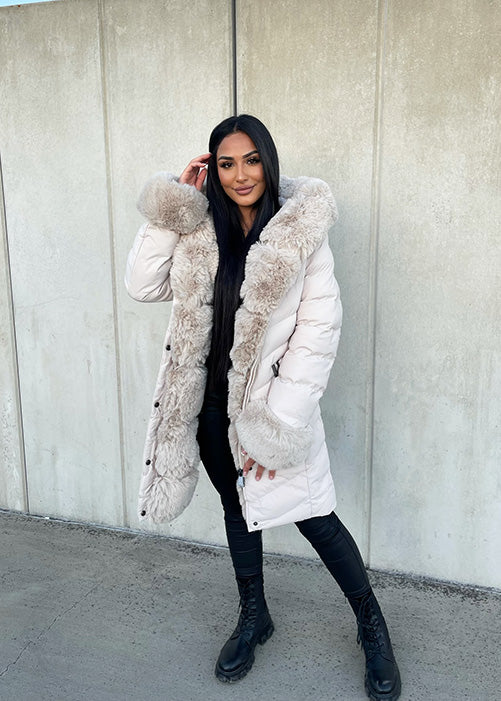 Modell trägt eine taillierte Damen Steppjacke mit Gürtel, Fellkragen und Fellärmeln – NAHA Wintermode