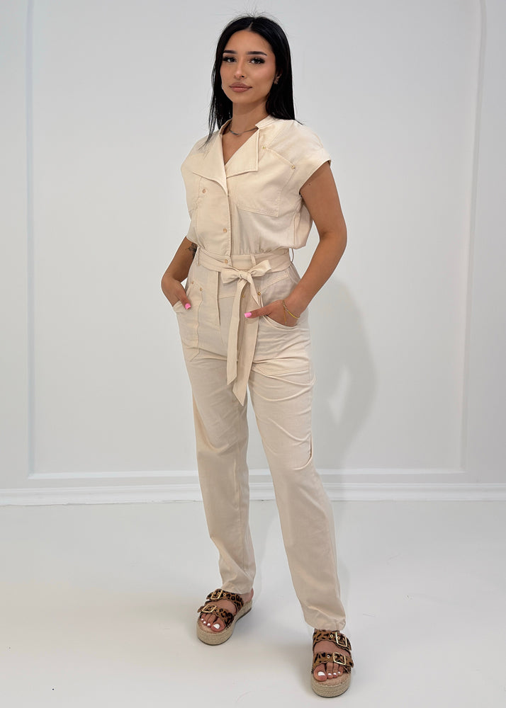 Frau trägt beigen Jumpsuit mit kurzen Ärmeln und Bindegürtel