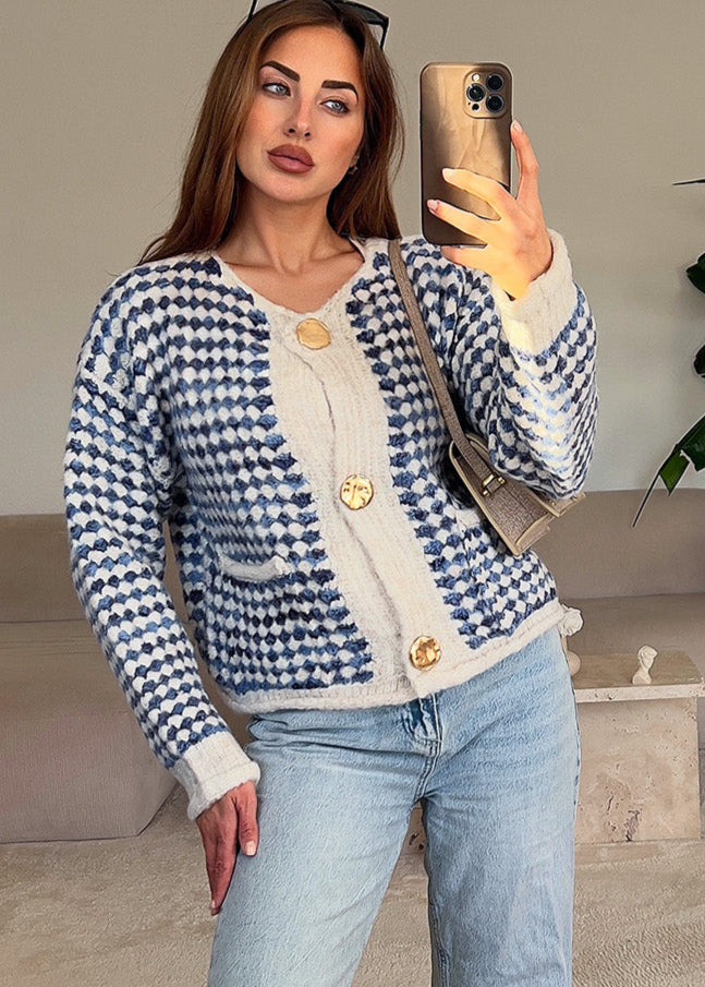 Modell trägt eine blaue Strickjacke mit goldenen Knöpfen und dekorativem Muster im modernen Schnitt