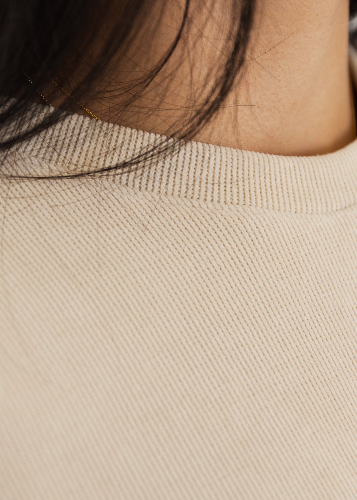 Detailansicht des feinen Strickmusters und der offenen Kante am Ausschnitt des beigen Pullovers