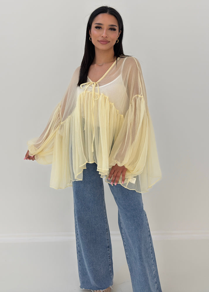 Frau trägt transparente Rüschenbluse mit weitem Schnitt, Volantärmeln & Bindeband – eleganter Sommerlook von NAHA