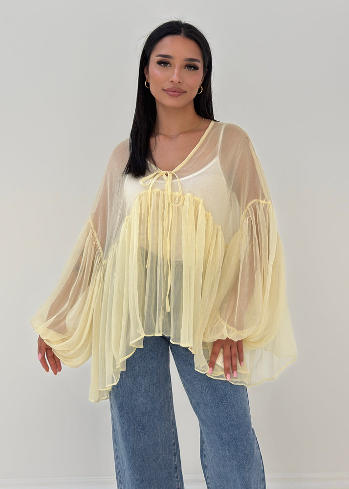 Frau trägt transparente Rüschenbluse mit weitem Schnitt, Volantärmeln & Bindeband – eleganter Sommerlook von NAHA