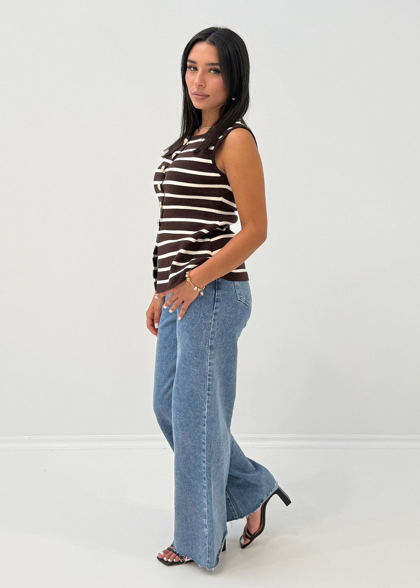 Modell trägt ärmellose, gestreifte Strickweste mit goldenen Knöpfen und Rundhalsausschnitt zu Jeans