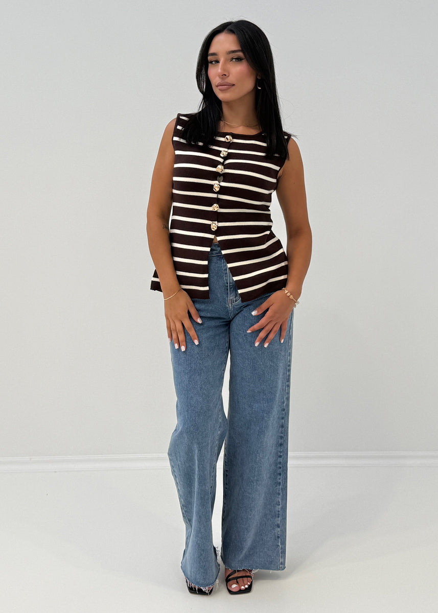 Modell trägt ärmellose, gestreifte Strickweste mit goldenen Knöpfen und Rundhalsausschnitt zu Jeans