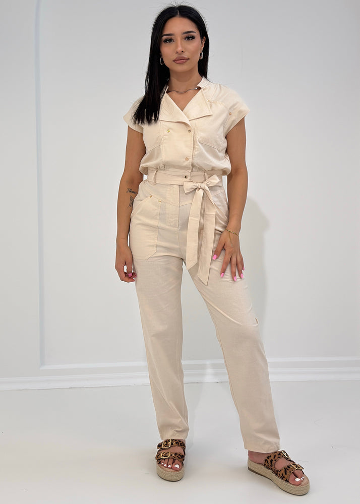 Frau trägt beigen Jumpsuit mit Gürtel in Weitansicht von vorn – Sommerlook aus der NAHA Kollektion