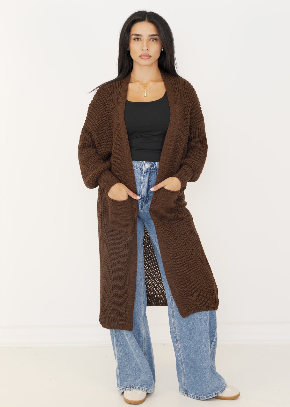 Lange Damen-Strickjacke in Braun offen getragen über schwarzem Top und Wide-Leg-Jeans