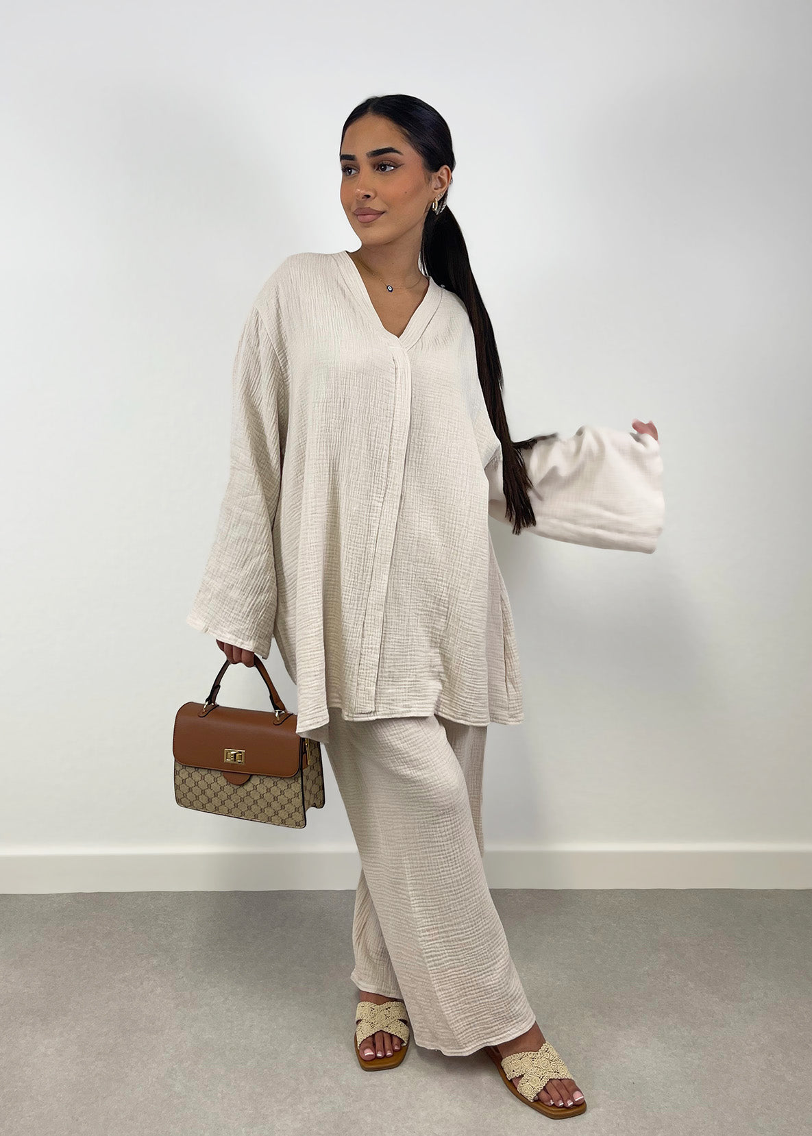 Frau trägt beigefarbenen Musselin-Zweiteiler mit Oversize-Bluse und weiter Hose, frontal fotografiert