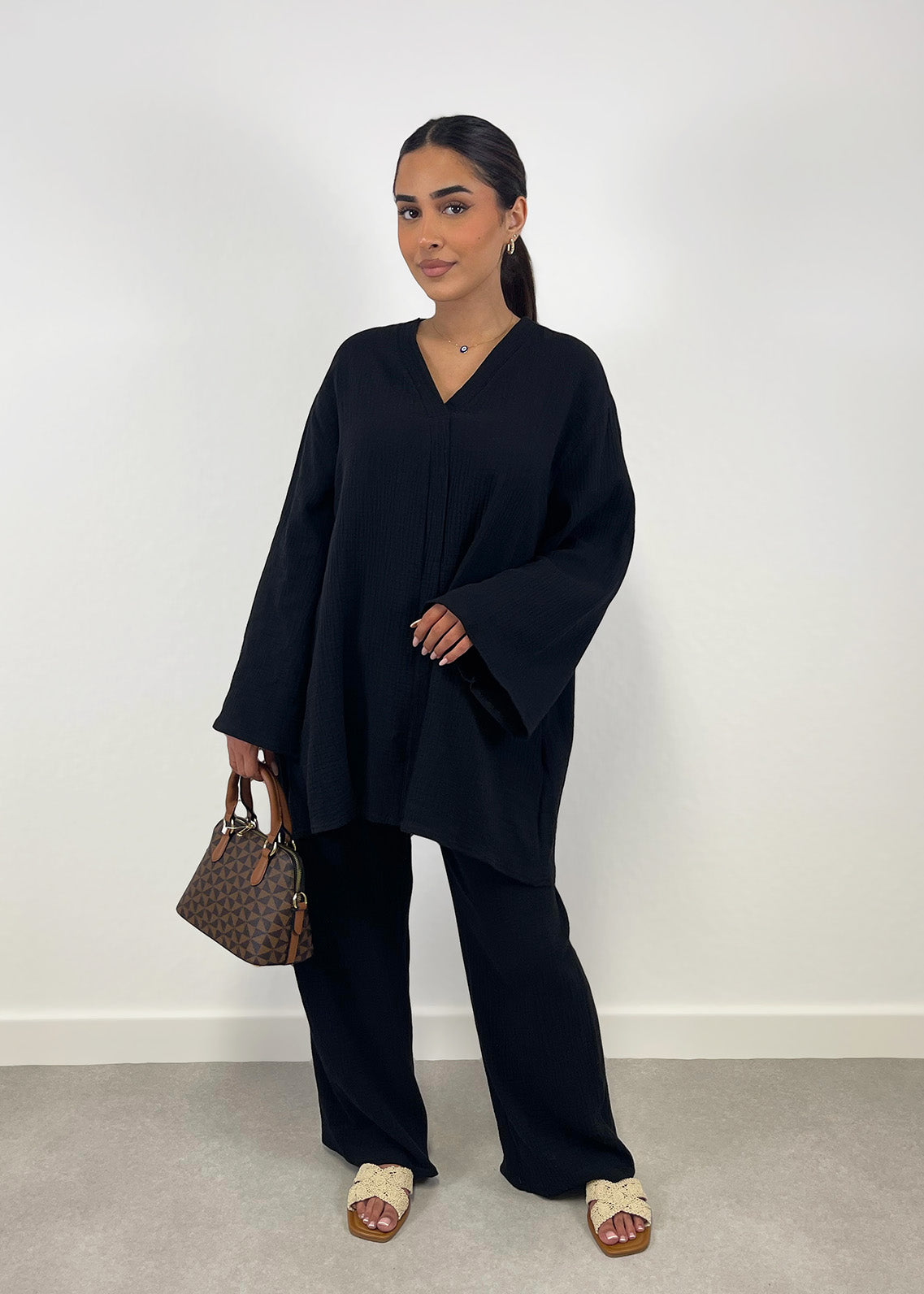 Frau trägt schwarzen Musselin-Zweiteiler mit Oversize-Bluse und weiter Hose, frontal fotografiert