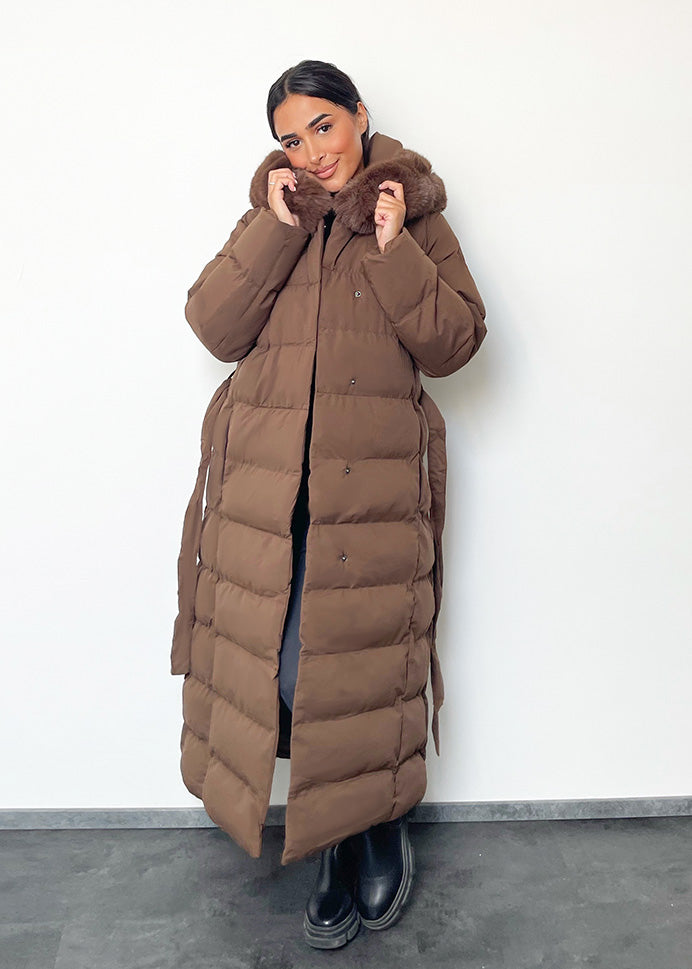 Modell trägt einen langen Damen Steppmantel mit Kapuze und Taillengürtel – NAHA Wintermode