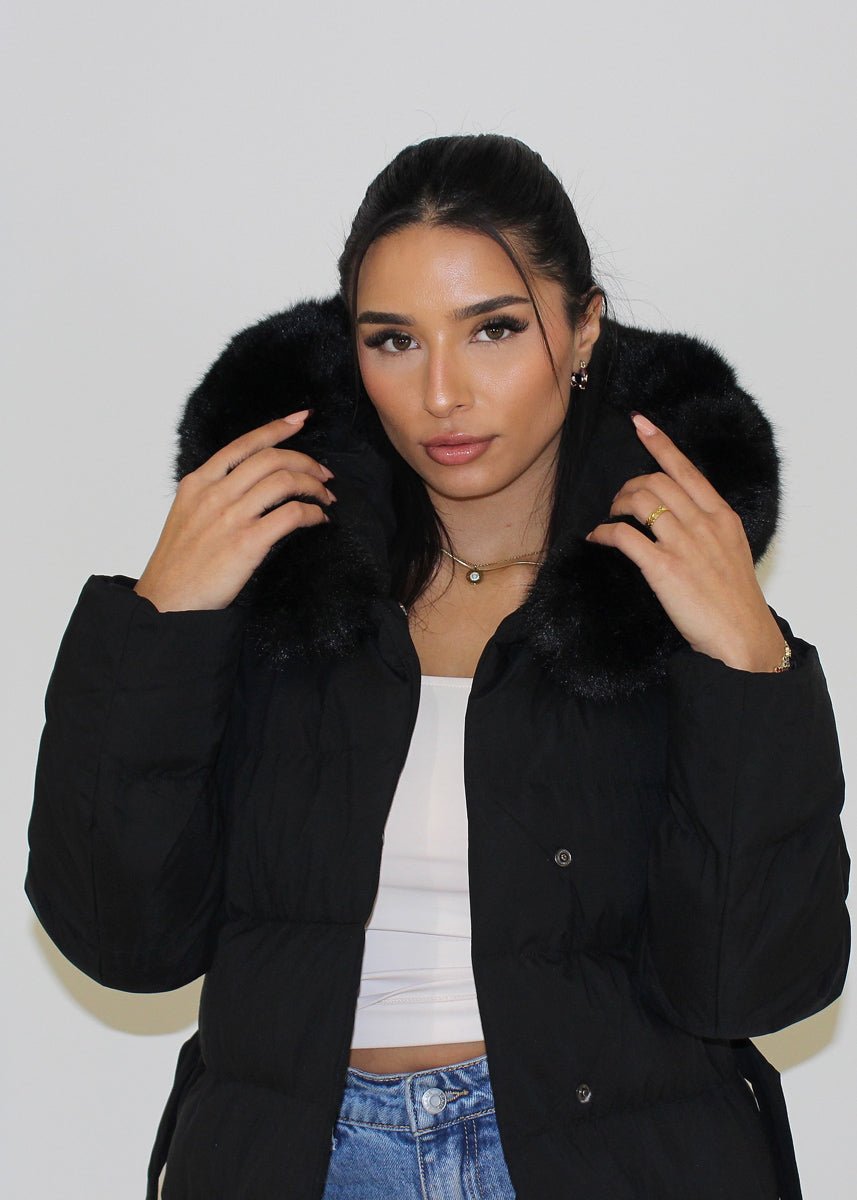 Modell trägt einen langen Damen Steppmantel mit Kapuze und Taillengürtel – NAHA Wintermode