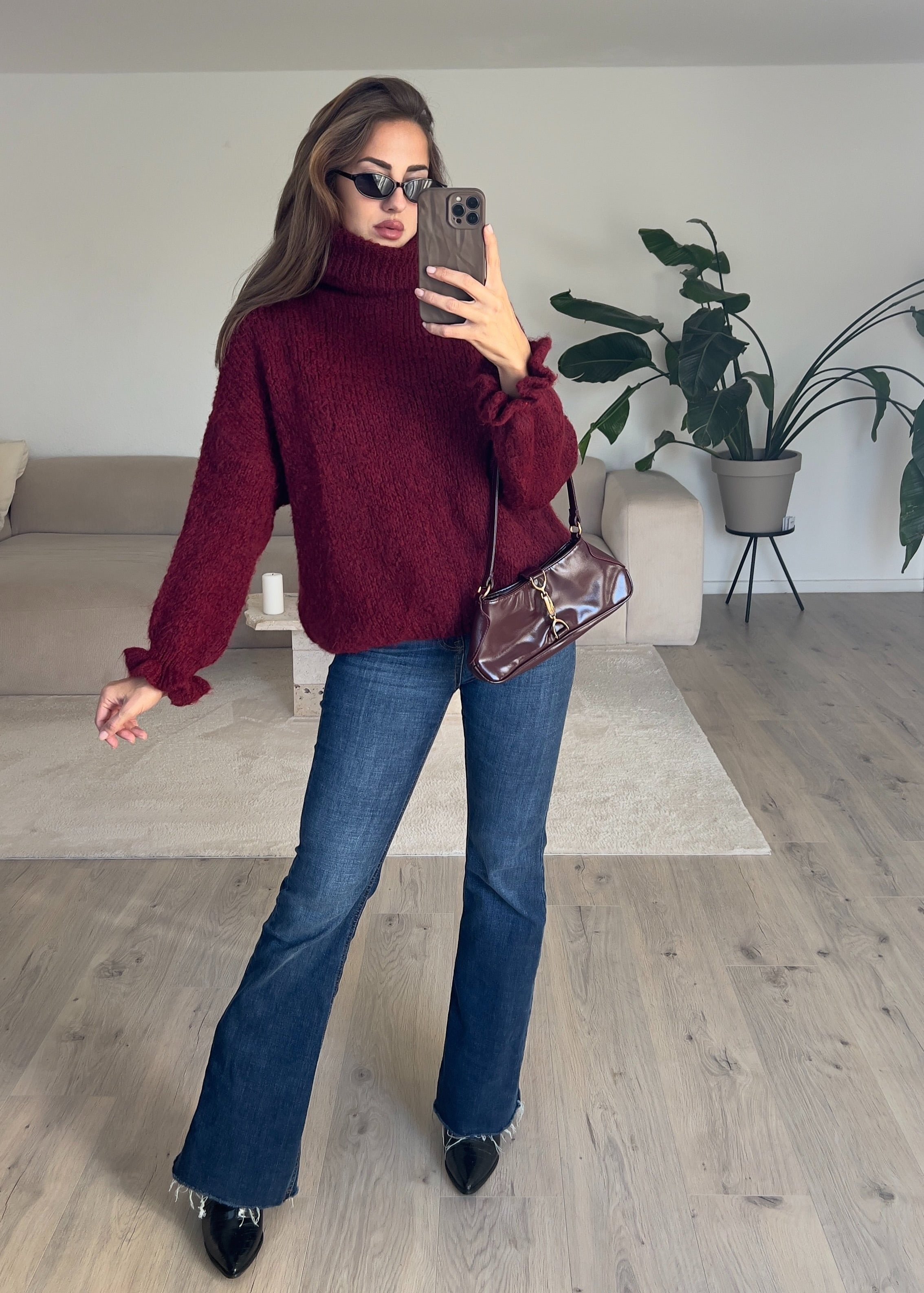Modell trägt einen dunkelroten Rollkragenpullover mit lockerer Passform und geripptem Kragen