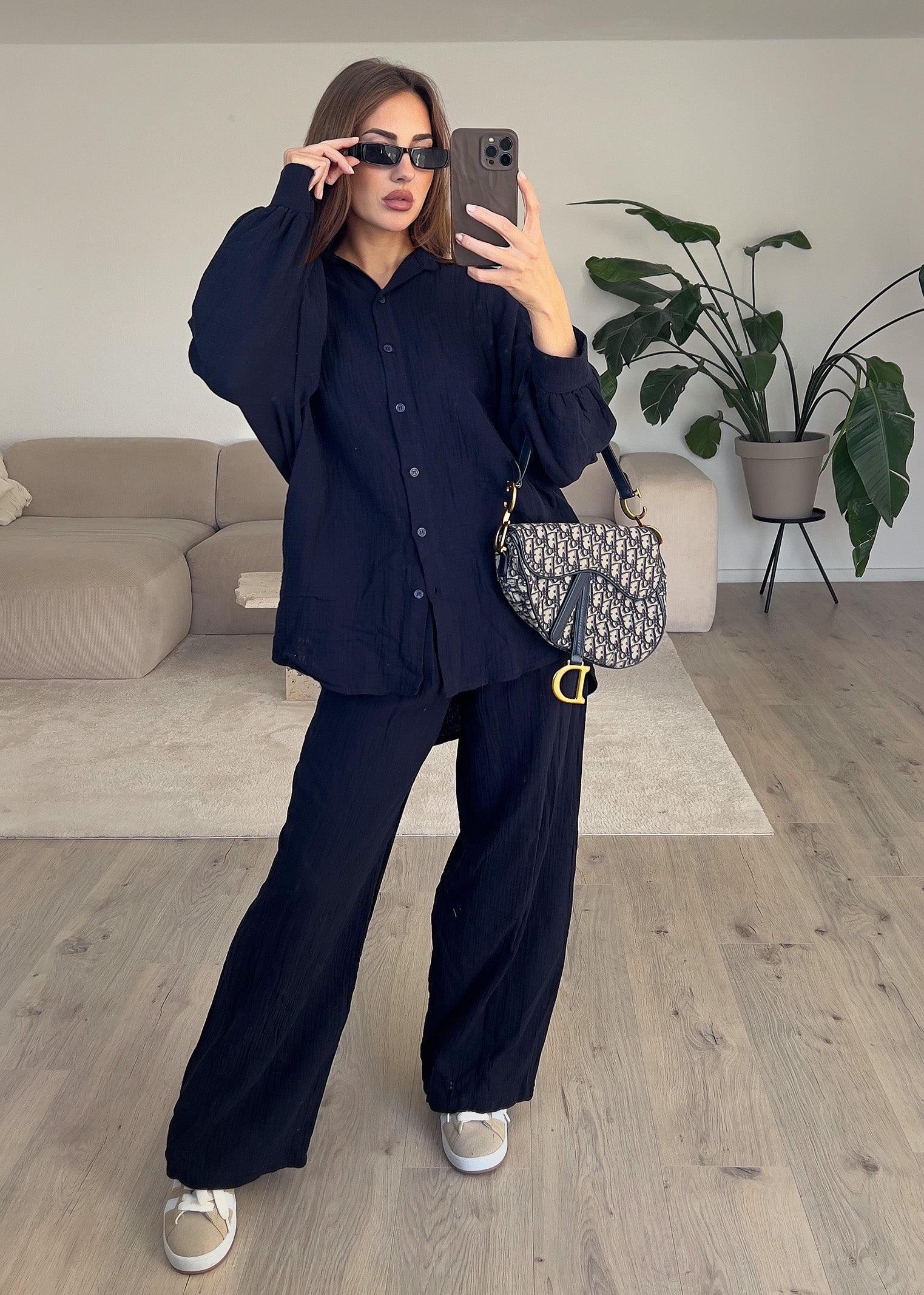 Modell trägt ein schwarzes Musselin-Zweiteiler-Set mit lockerem Oversize-Hemd und elastischer Hose