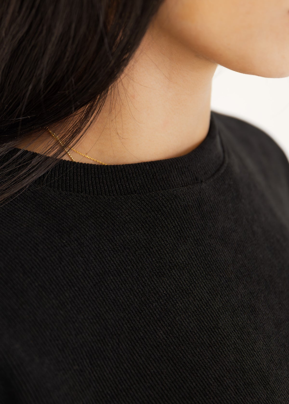 Detailansicht des schwarzen Strickstoffs in Cord-Optik am Ausschnitt mit Goldschmuck