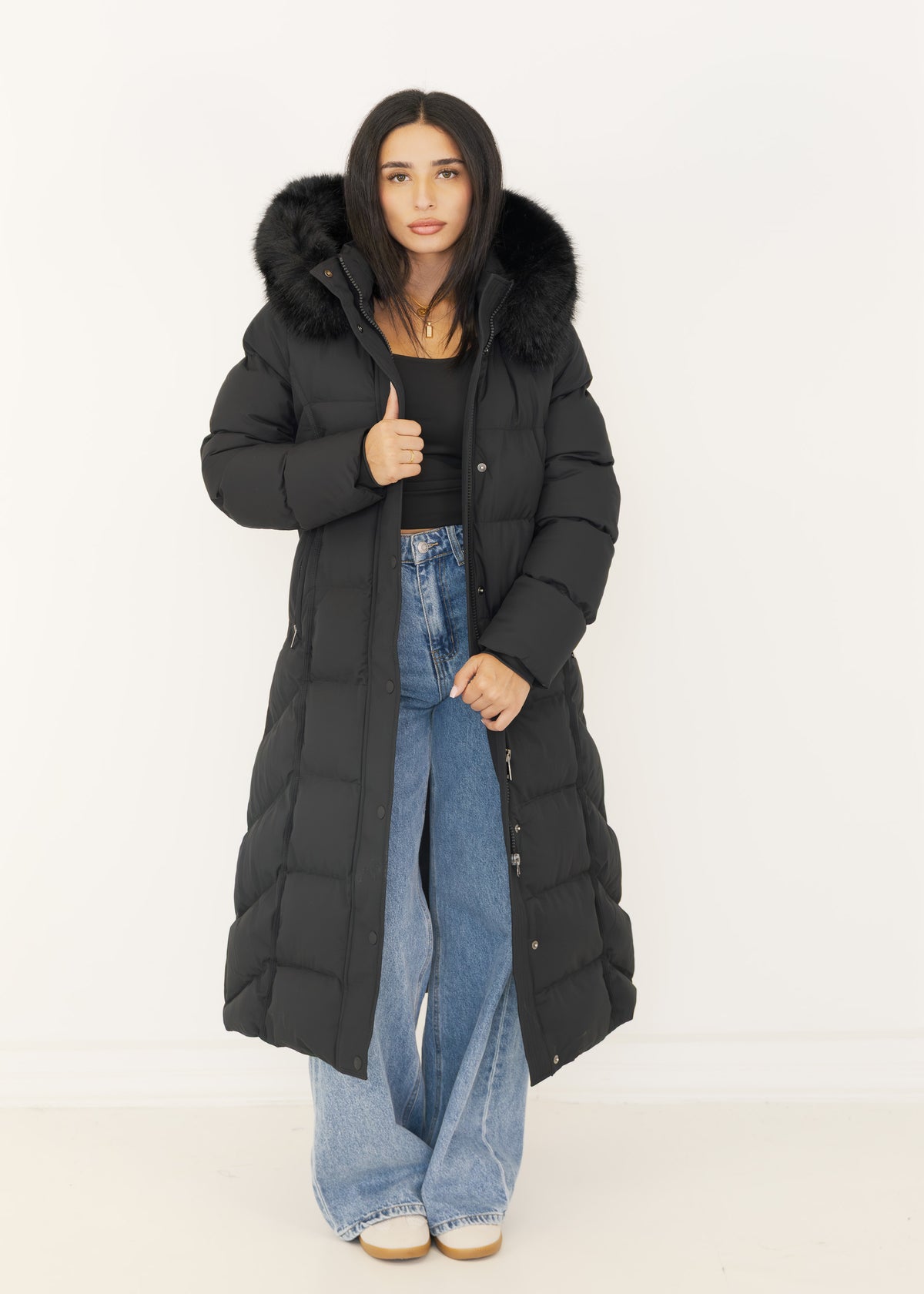 Model hält den offenen schwarzen Wintermantel mit Fellkapuze am Revers