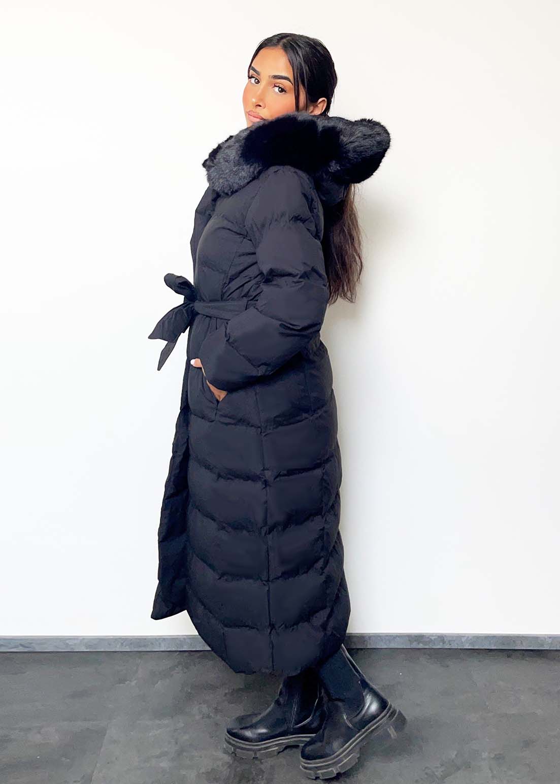 Modell trägt einen langen Damen Steppmantel mit Kapuze und Taillengürtel – NAHA Wintermode