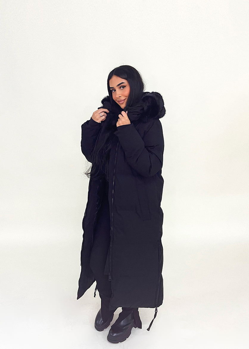 Modell trägt einen langen Damen Steppmantel mit Kapuze und seitlichen Reißverschlüssen – NAHA Wintermode