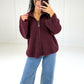 Frau in bordeauxroter Oversize-Strickjacke mit Reißverschluss und Stehkragen zu Jeans