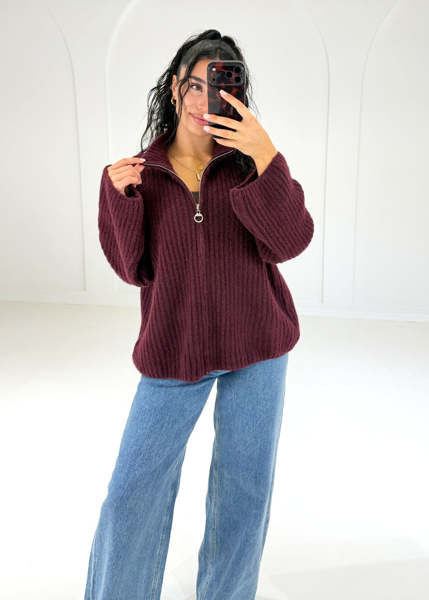 Frau in bordeauxroter Oversize-Strickjacke mit Reißverschluss und Stehkragen zu Jeans