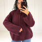 Frau in bordeauxroter Oversize-Strickjacke mit Reißverschluss und Stehkragen zu Jeans