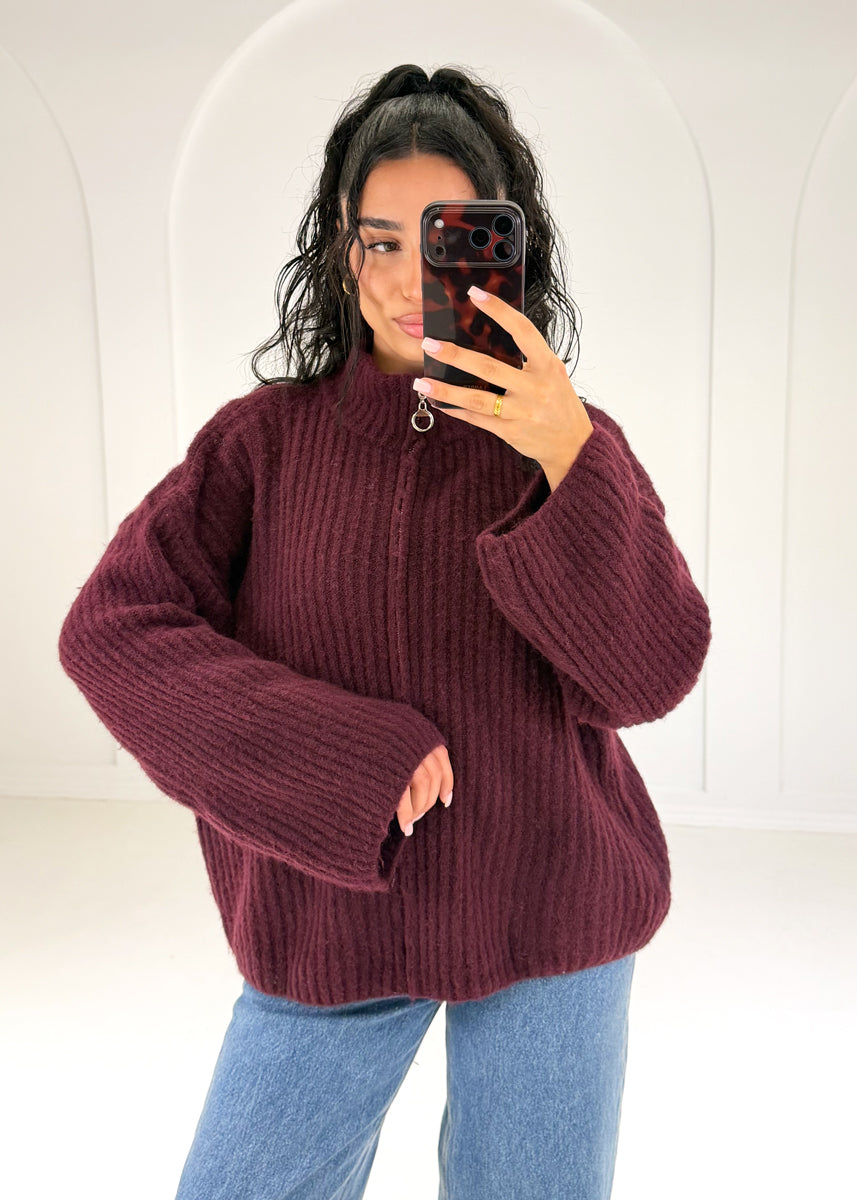 Frau in bordeauxroter Oversize-Strickjacke mit Reißverschluss und Stehkragen zu Jeans