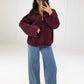 Frau in bordeauxroter Oversize-Strickjacke mit Reißverschluss und Stehkragen zu Jeans