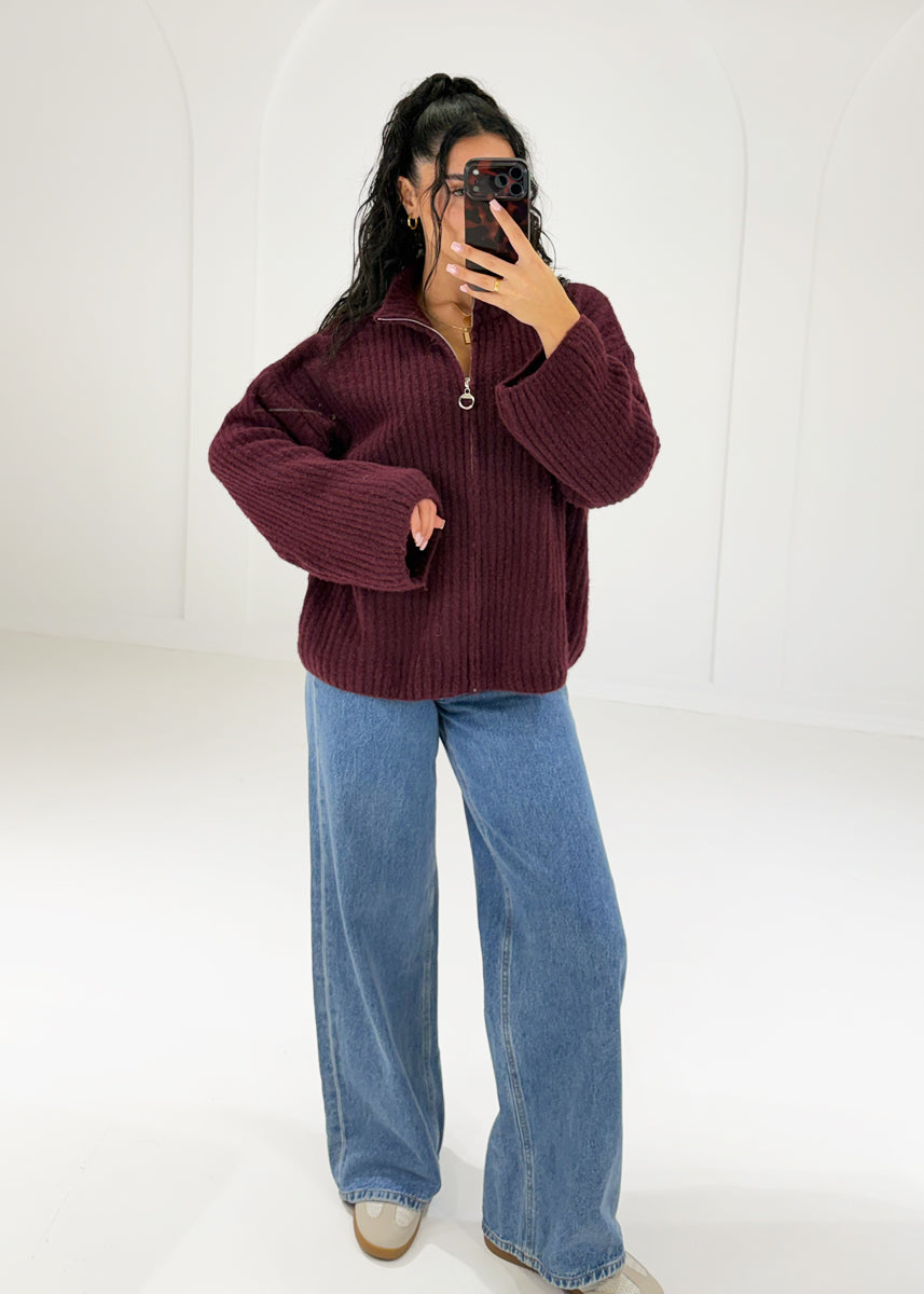 Frau in bordeauxroter Oversize-Strickjacke mit Reißverschluss und Stehkragen zu Jeans