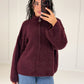 Frau in bordeauxroter Oversize-Strickjacke mit Reißverschluss und Stehkragen zu Jeans