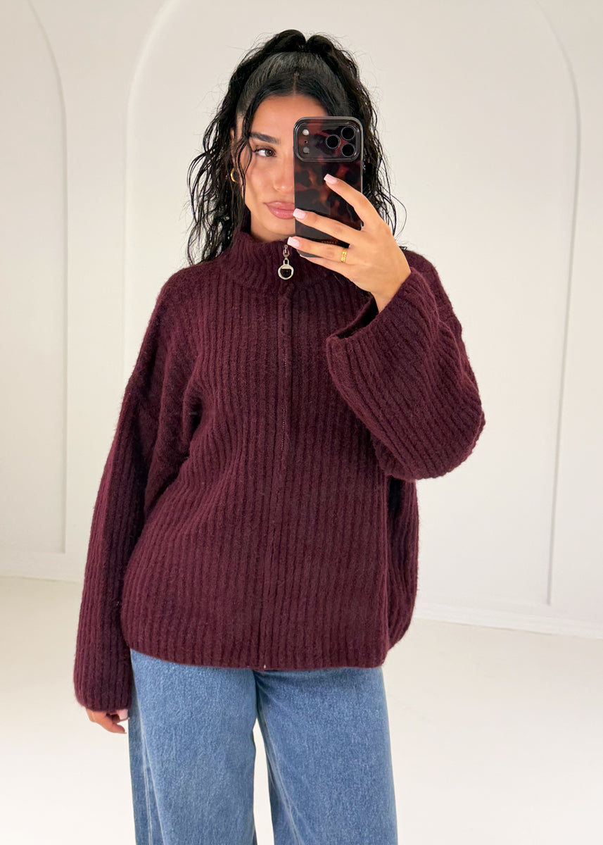 Frau in bordeauxroter Oversize-Strickjacke mit Reißverschluss und Stehkragen zu Jeans