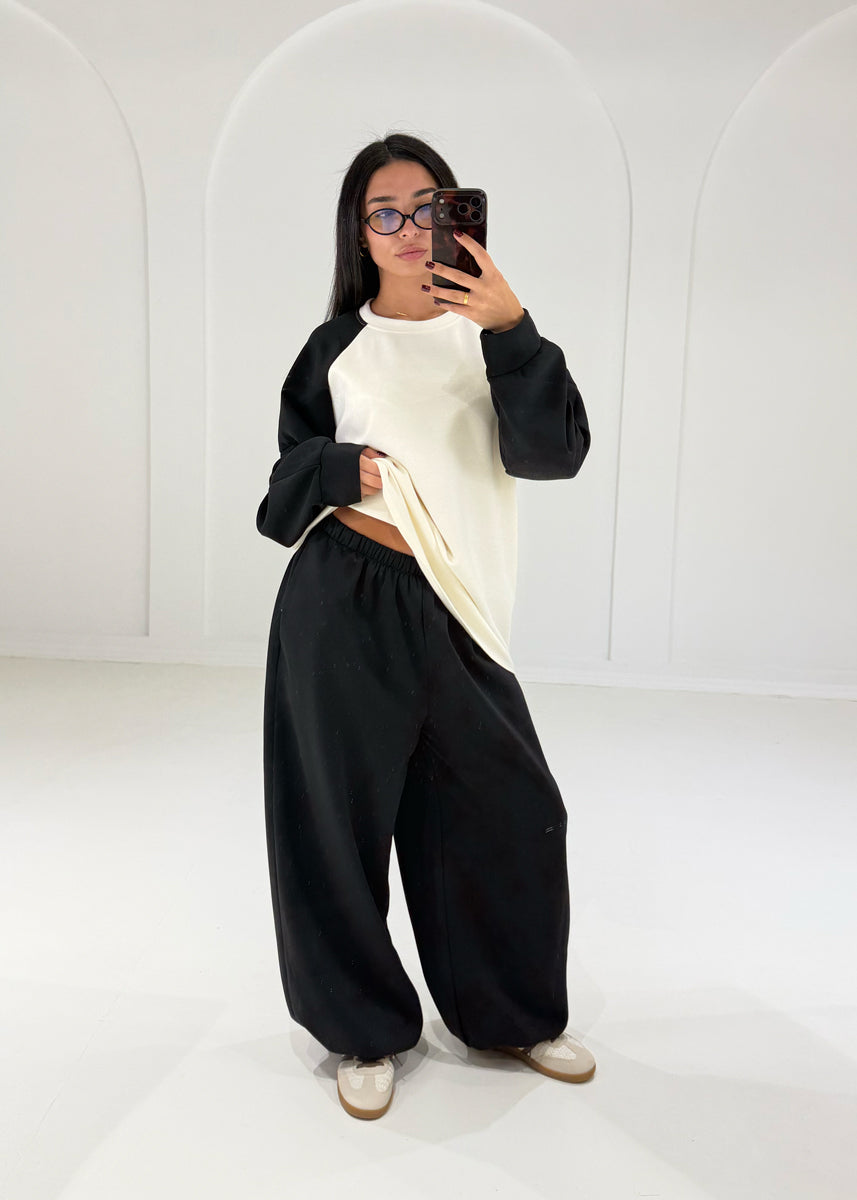 Model hebt das Sweatshirt an und zeigt den elastischen Bund der schwarzen Ballonhose