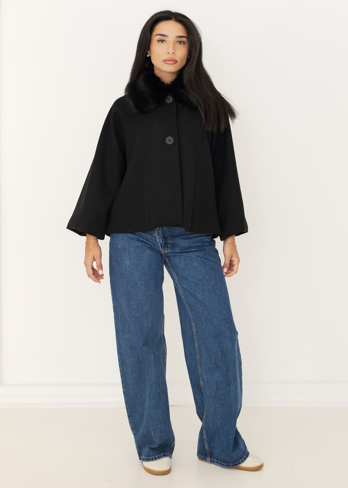 Damen Cape-Jacke in Schwarz mit Kunstfellkragen, geknöpft getragen zu blauer Wide-Leg-Jeans