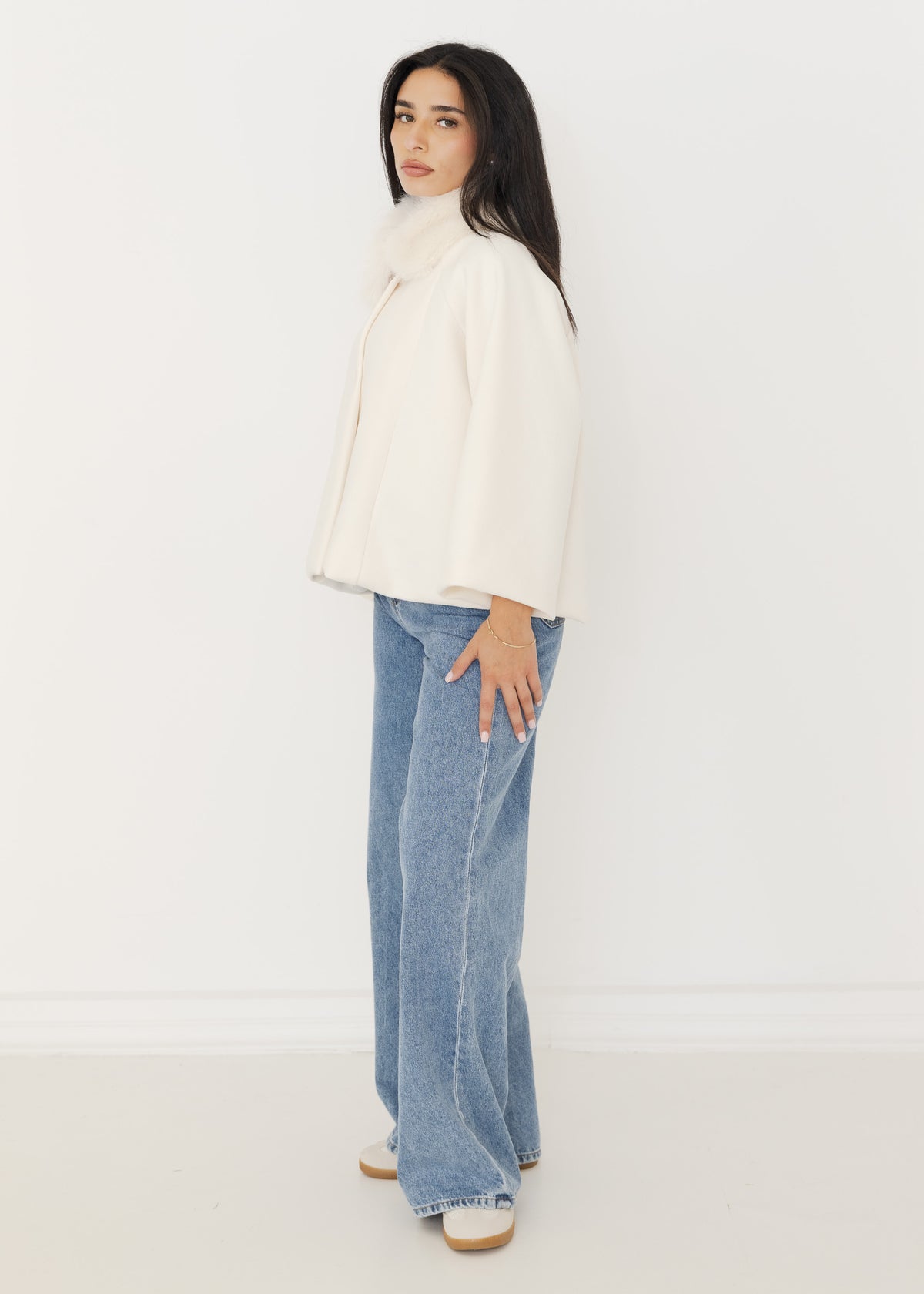 Seitenansicht der cremefarbenen Capejacke mit weiten Ärmeln und cropped Länge