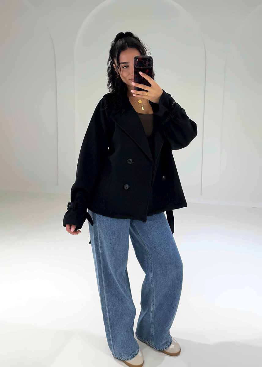 Schwarzer kurzer Trenchcoat offen getragen über braunem Top, Oversize-Look