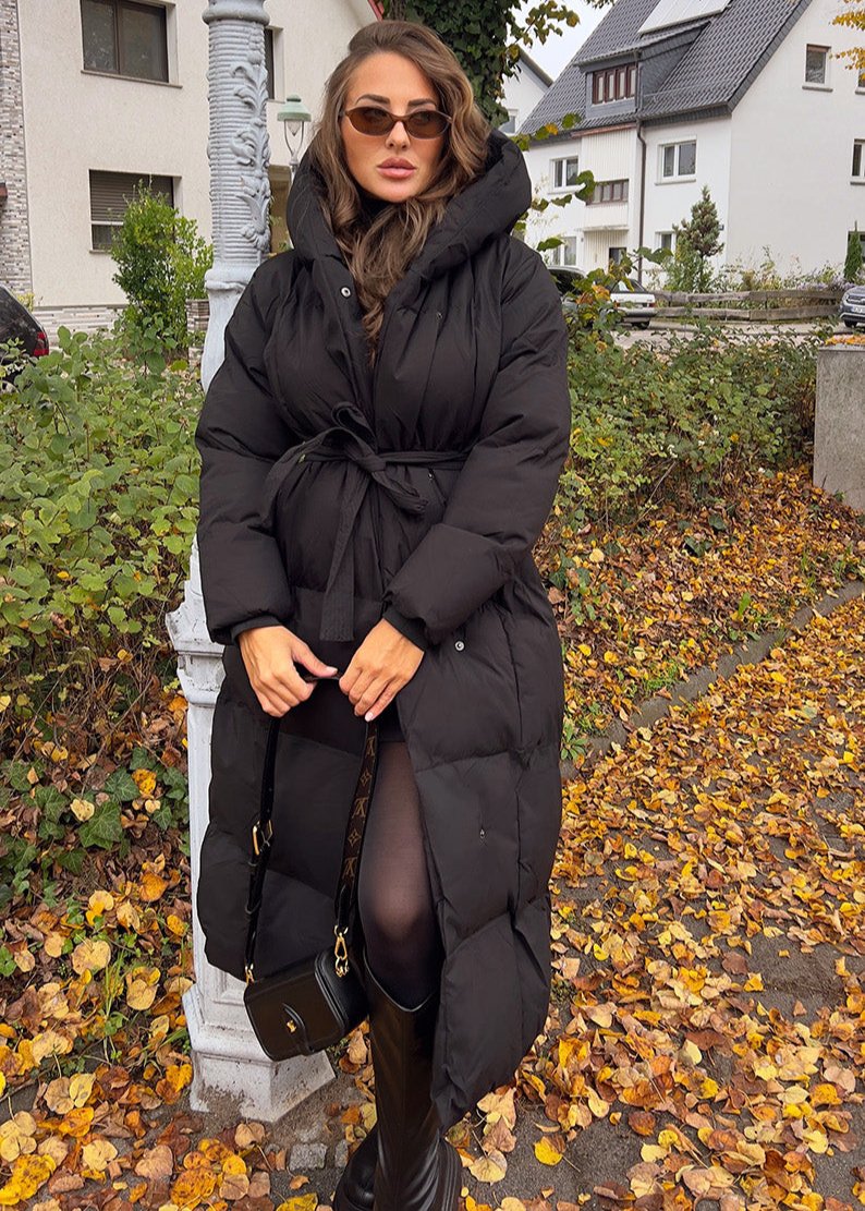 Modell trägt langen schwarzen Damen Steppmantel mit Kapuze und Taillengürtel in Frontansicht – NAHA Winterjacke