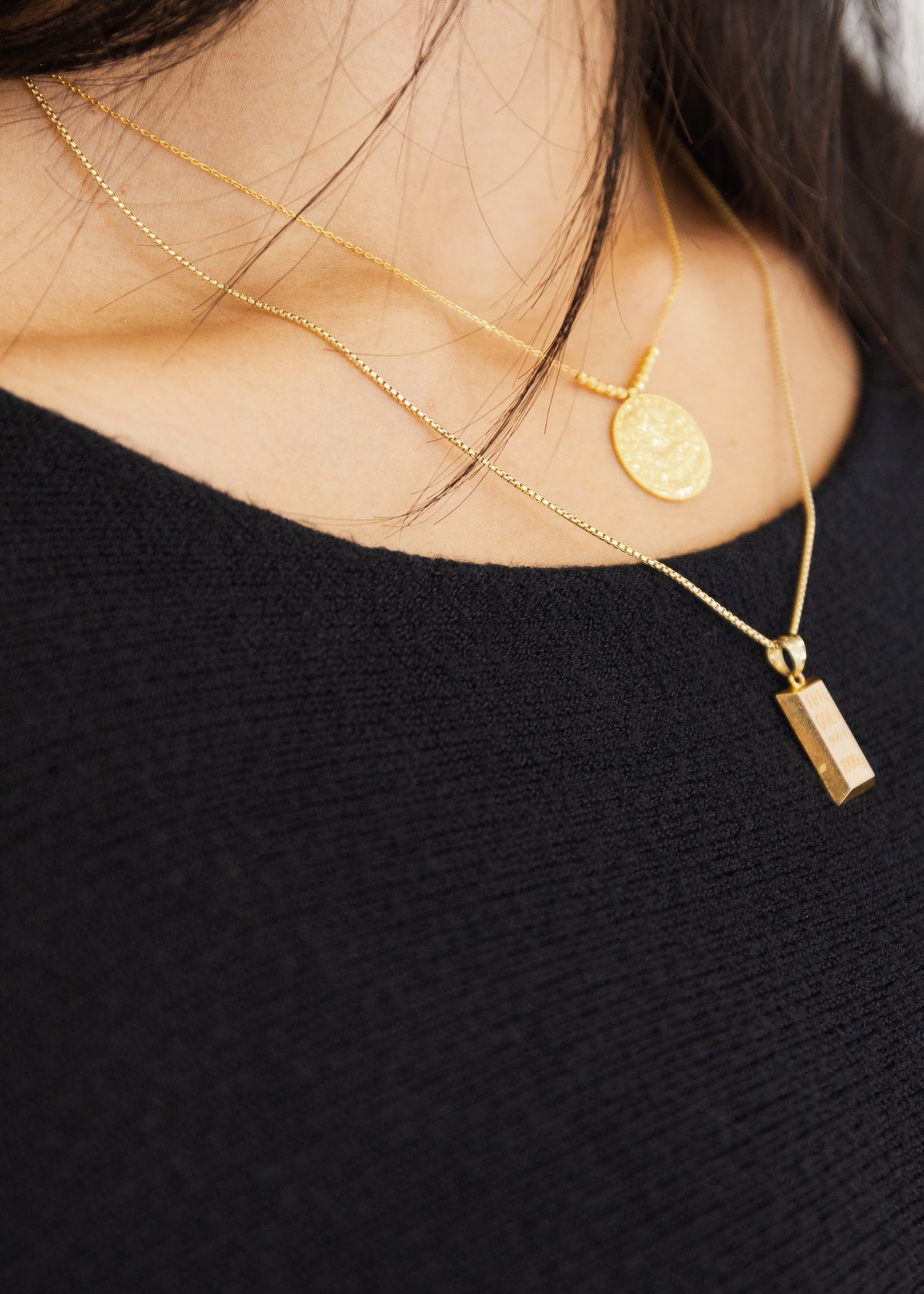 Detailansicht des schwarzen Feinstricks am Ausschnitt mit Goldschmuck