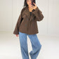 Frau in kurzer schokobrauner Caban Jacke mit Zweireiher-Knöpfen und großem Revers kombiniert mit Wide Leg Jeans und schwarzem Top
